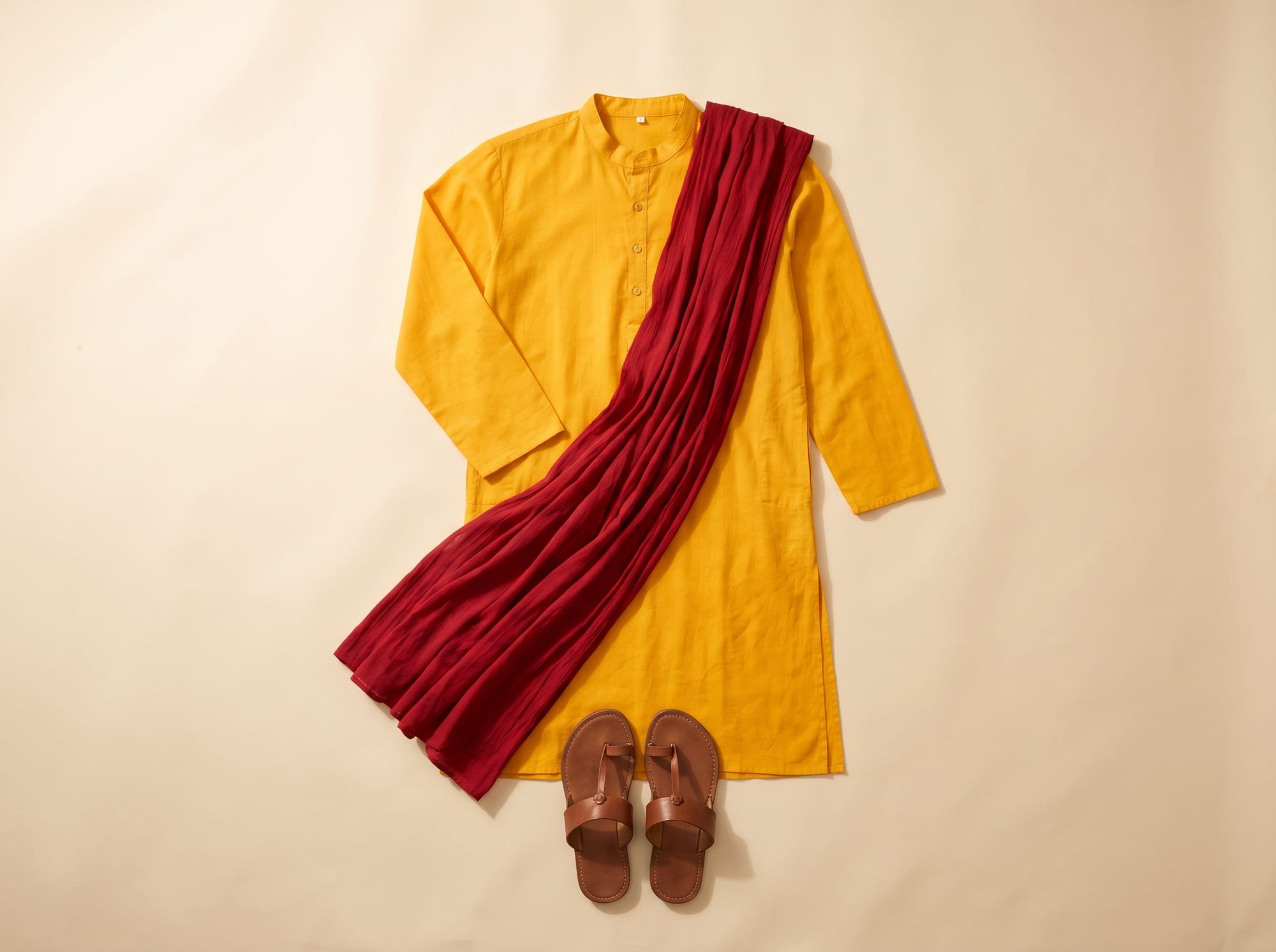 Flat lay of a yellow kurta with a red dupatta and brown leather chappals.