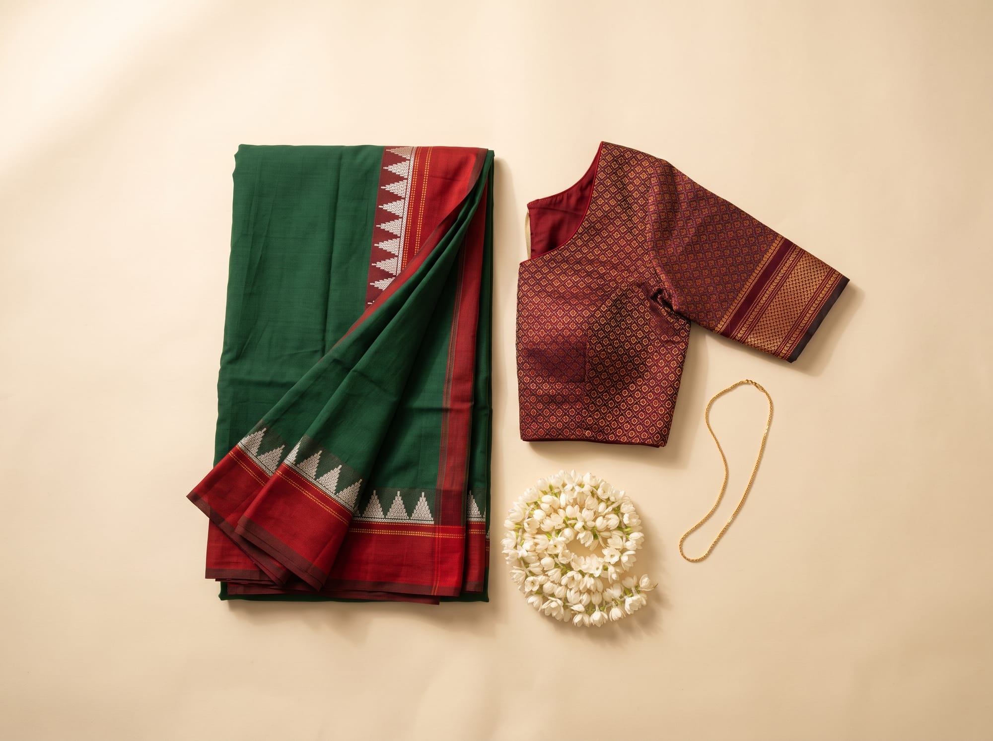 Flat lay of an Ilkal saree with a red pallu, a khana blouse, jasmine and a gold chain.