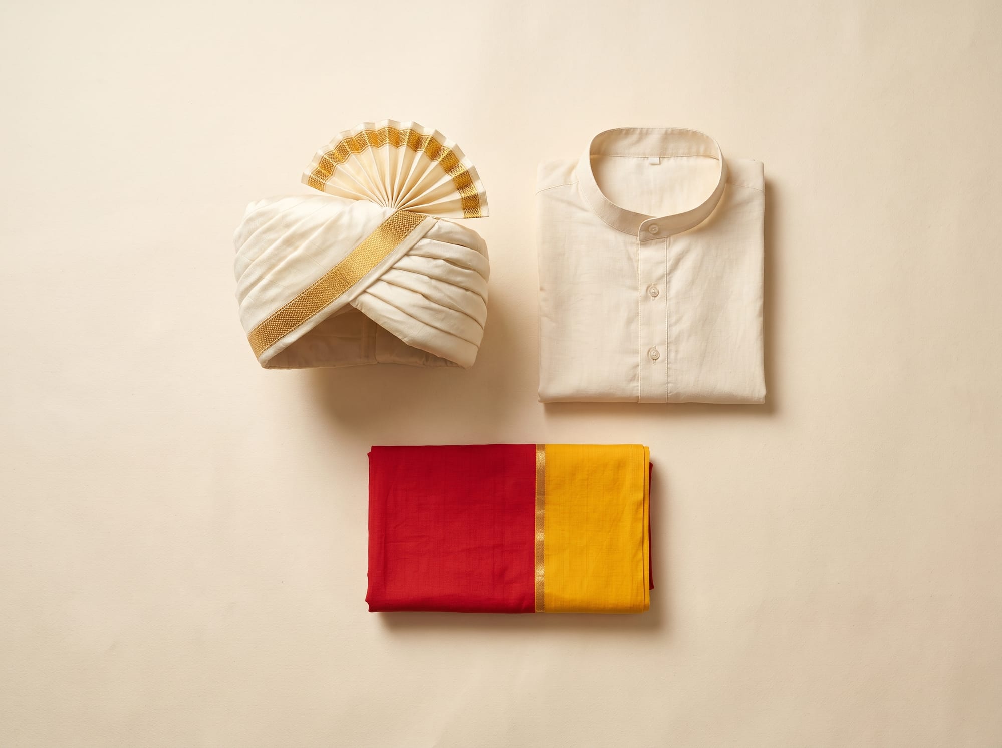 Flat lay of an ivory Mysore peta with a gold band, a cream kurta and a red-and-yellow shalya.